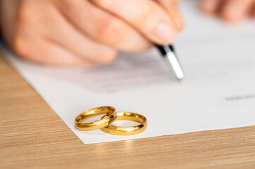 Divorce, rings and signature on paperwork for a lawyer, register wedding or writing on a contract. Table, closeup and a certificate, planning or legal documrnts for a commitment or engagement