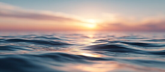 Obraz premium Gentle ocean waves at sunset. Soft, blurry water surface reflecting golden, peach-toned sunset light, with hazy clouds. A close-up view shows the texture of rippling water