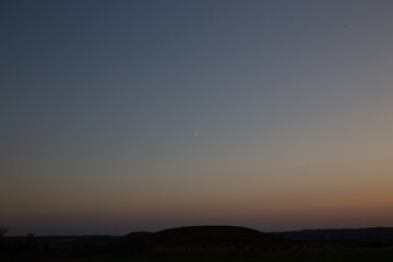 A crescent moon rises in a colorful dusk sky over the tranquil landscape.