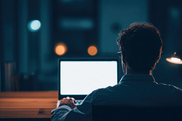 A man working on a laptop at night, illuminated by the screen's glow, with a warm ambiance from nearby light sources.