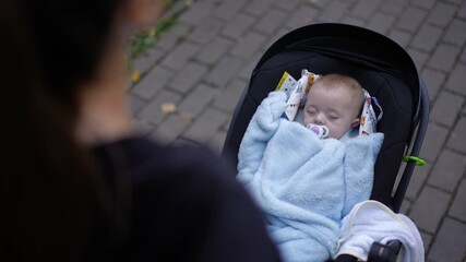 A tranquil moment of a sleeping baby in a stroller, wrapped snugly in a blue blanket, enjoying the fresh air.