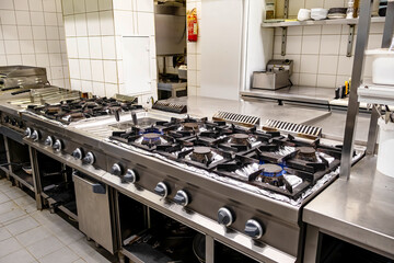Large stainless steel cooking range with ten active gas burners in commercial kitchen
