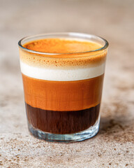 A visually appealing layered coffee drink in a clear glass, showcasing distinct brown and cream colors.