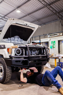 man lying under car installing bull bar onto vehicle in mechanic workshop