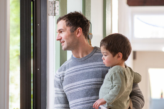 A man in a striped sweater holds a baby boy,  at the front door. - Powered by Adobe