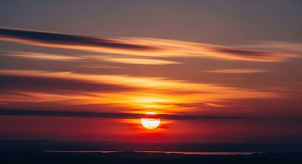 Vibrant red sun sinking below dramatic dark clouds during a serene and beautiful evening sunset over the horizon