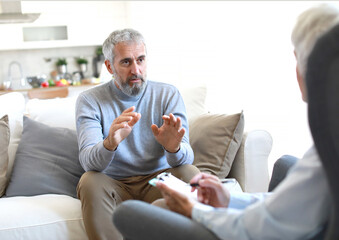 Portrait of a senior mature or mid aged man looking thoughtful or stressed and sad while sitting in session with his female therapist