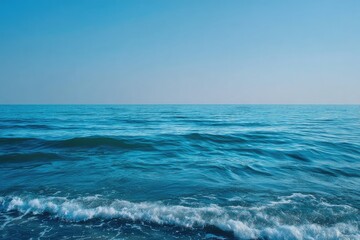 Fototapeta premium Wide shot of a tranquil ocean. Clear, vibrant blue water meets a serene, cloudless sky. Gentle waves lap at the shore