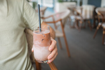 Close-up of a man sitting at table on summer terrace and enjoying refreshing iced latte coffee. 