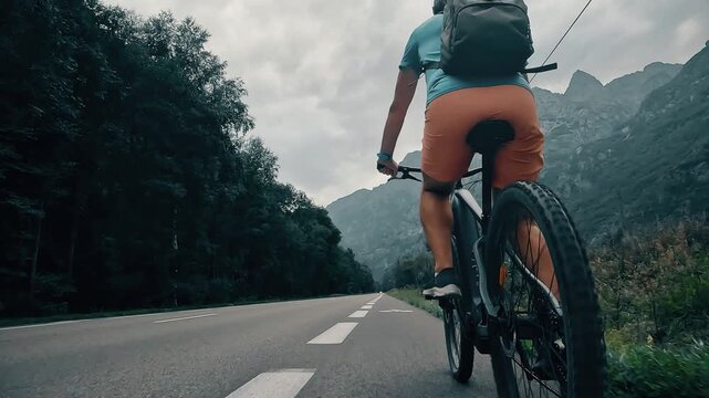 Rear view of a cyclist riding on a road in the French Alps, camera following behind the rider. Scenic mountain landscape