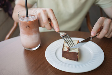 Close-up of a man enjoying a slice of cheesecake and a glass of iced latte coffee, while sitting on the terrace of a cafe.