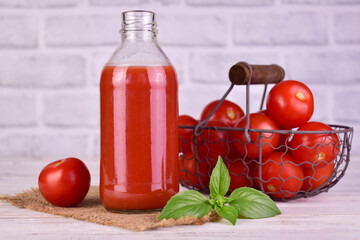 Tomato juice in a bottle and fresh tomatoes in a basket in the background.

