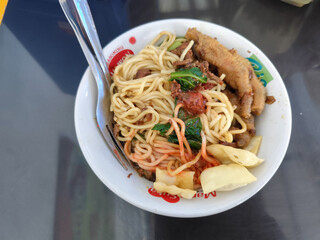 A complete bowl of chicken noodles with claws, dumplings, chicken pieces and red chili sauce on top, traditional Indonesian food.