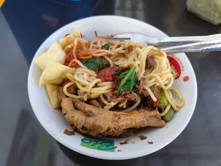 A complete bowl of chicken noodles with claws, dumplings, chicken pieces and red chili sauce on top, traditional Indonesian food.