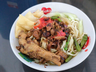 A complete bowl of chicken noodles with claws, dumplings, chicken pieces and red chili sauce on top, traditional Indonesian food.