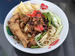 A complete bowl of chicken noodles with claws, dumplings, chicken pieces and red chili sauce on top, traditional Indonesian food.
