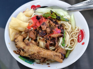 A complete bowl of chicken noodles with claws, dumplings, chicken pieces and red chili sauce on top, traditional Indonesian food.