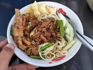 A complete bowl of chicken noodles with claws, dumplings, chicken pieces and red chili sauce on top, traditional Indonesian food.