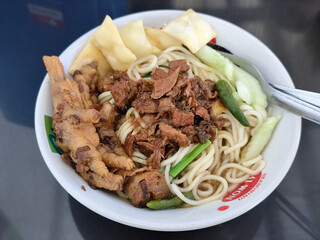 A complete bowl of chicken noodles with claws, dumplings, chicken pieces and red chili sauce on top, traditional Indonesian food.