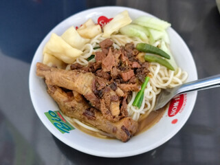 A complete bowl of chicken noodles with claws, dumplings, chicken pieces and red chili sauce on top, traditional Indonesian food.