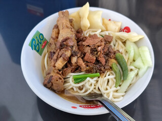 A complete bowl of chicken noodles with claws, dumplings, chicken pieces and red chili sauce on top, traditional Indonesian food.