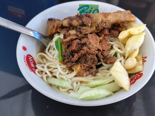 A complete bowl of chicken noodles with claws, dumplings, chicken pieces and red chili sauce on top, traditional Indonesian food.