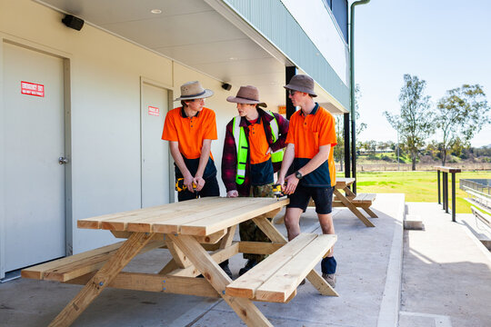 Three teen trade apprentices standing by picnic table constructed in hands on learning course