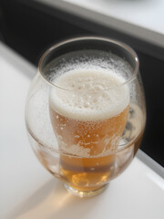 A glass filled with amber beer with a frothy white head,