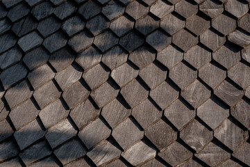 Abstract background of gray hexagonal wooden roof shingles. Close-up of a traditional wood tile pattern with natural texture and strong shadows.
