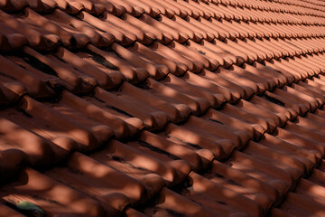 Fototapeta premium Close-up texture of traditional terracotta roof tiles with sunlight and shadow. Abstract background of a classic orange clay rooftop pattern.