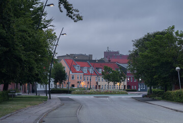 Picturesque street with colorful houses and lush trees in Thisted, Denmark. Urban greenery, residential architecture, and tranquil small-town atmosphere on a cloudy summer evening in Jutland