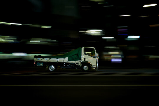 夜の車道を走り抜ける白い中型トラックのスピード感