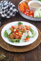 fresh chicken salad with cucumber, tomatoes, carrot, and corn on white plate
