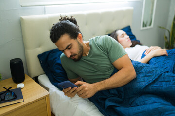 Man using smartphone while partner sleeping in bed