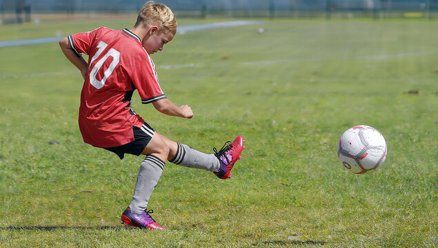Young boy aged 10, wearing a red football shirt, gray socks and football boots, takes a free kick. generative AI