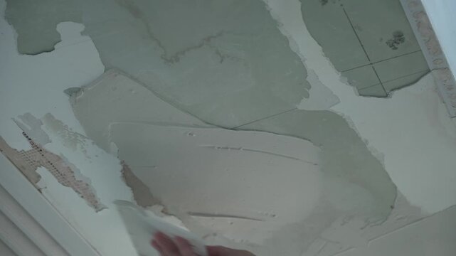 Close-up of wall surface during putty application showing unfinished plaster layer with cracks and peeling