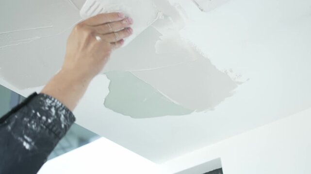 Worker's hand applying putty on ceiling during interior renovation construction
