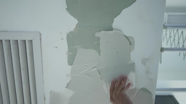 Hand peeling off damaged wall paint during interior renovation and repair work