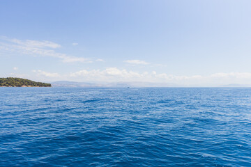 Expansive view of deep blue Mediterranean sea with forested island coastline, white clouds, and...