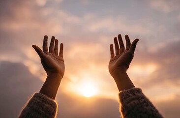 Hands raised in prayer against a colorful sunset sky