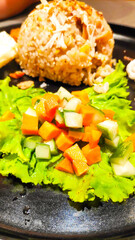 Close up photo of indonesian fried rice served with sunny side up, crackers and pickles on black plate
