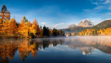 Fototapeta premium golden autumn trees alongside a misty lake with mountain backdrop scenic fall landscape reflecting in water for tranquil nature backgrounds