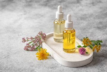 Cosmetic serum or essential oil in dropper bottles with wild flowers on white ceramic tray, selective focus, cosmetic products, beauty and health concept