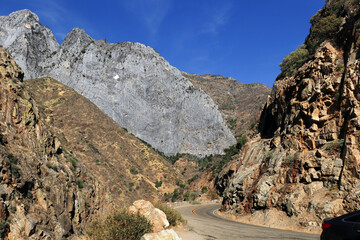 A mountain road in California, USA, going into the mountains. There is a bright blue sky in the background