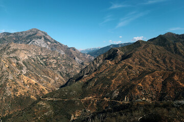 The mountains are covered with small green vegetation. On one of the mountains, a road can be seen going deep into the ridge. The photo was taken in clear sunny weather
