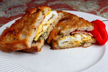 A savory breakfast grilled cheese sandwich with Canadian bacon, fried eggs, American cheese, sauteed jalapenos on grilled cheddar-jalapeno sour dough bread.