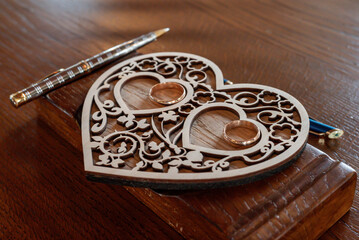 Carved wooden decorative bowl in the shape of a heart with two circular slots holding wedding rings, symbolizing love and marriage.