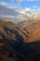 Mountain landscape before sunset. The mountains have a slightly yellow tint due to the setting Sun. The sky is covered with a lot of clouds