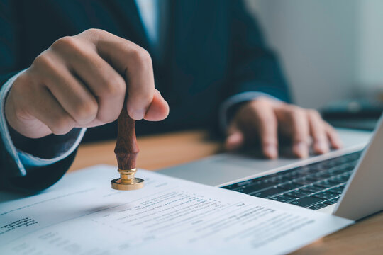 Businessman stamping approval on official document with laptop, legal contract validation certification agreement paperwork authorization business approval process and corporate compliance.