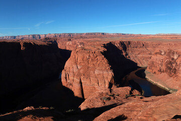 The bend of the Colorado River in the Grand Canyon. A mountain range is visible from behind. The photo was taken in the morning in clear sunny weather